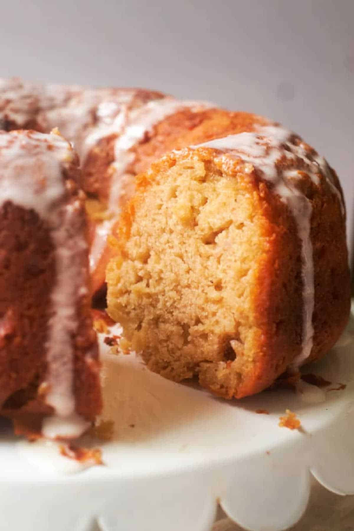 A sliced Banana Bread Bundt Cake with white icing drizzled on top, displayed on a white cake stand.