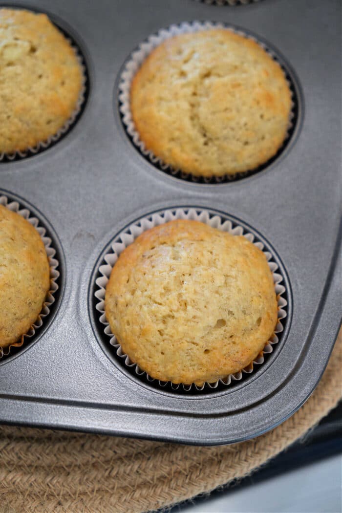 Freshly baked banana muffins in paper liners sit inside a metal muffin pan, ready to enjoy with your favorite banana muffin recipe.