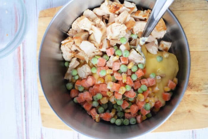 A metal bowl with chopped chicken, frozen mixed vegetables, creamy soup, and Bisquick on a wooden cutting board—perfect for making Chicken and Dumplings.