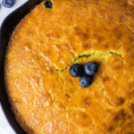 Golden cornbread baked to perfection—this jiffy cornbread in a cast iron skillet is topped with three fresh blueberries in the center.
