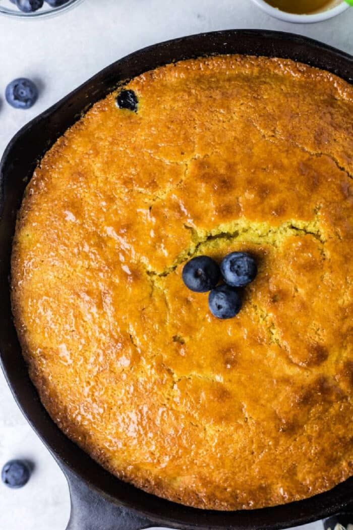 Golden cornbread baked to perfection—this jiffy cornbread in a cast iron skillet is topped with three fresh blueberries in the center.