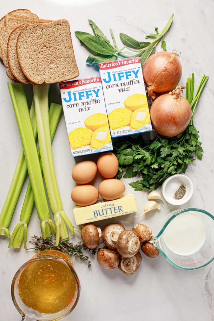 Ingredients for stuffing laid out: bread, Jiffy Cornbread mix, eggs, butter, celery, onions, mushrooms, herbs, broth, and milk—perfect for a flavorful Cornbread Stuffing.