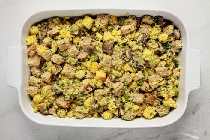 A casserole dish filled with Jiffy cornbread stuffing mixed with vegetables and herbs, ready to be baked.