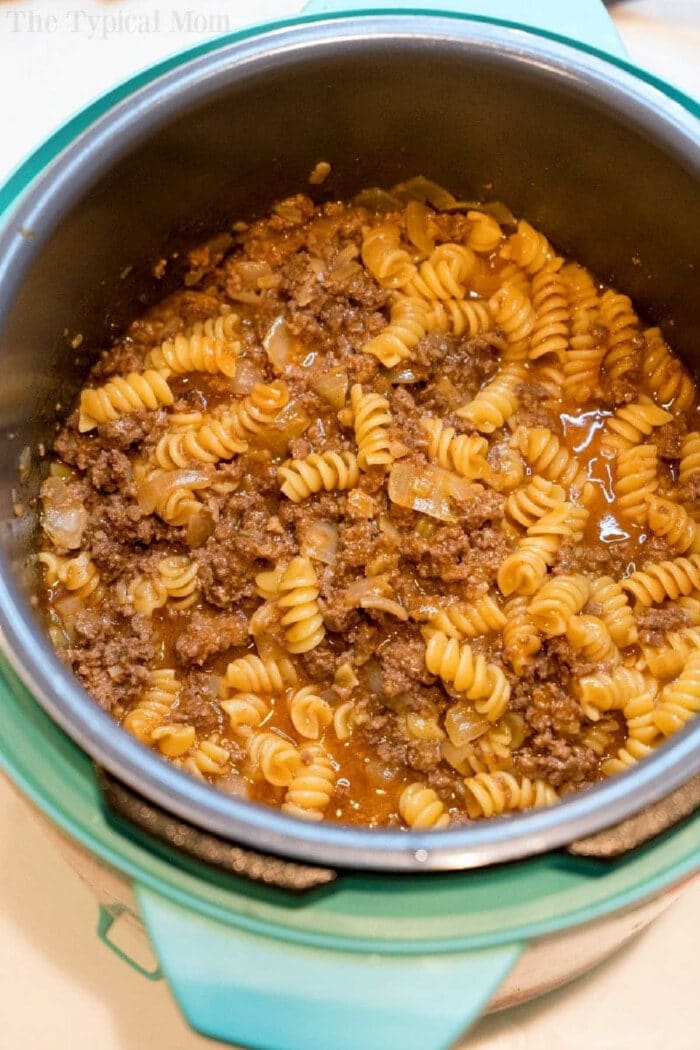 Cooked rotini pasta with ground beef and sauce in a teal pressure cooker, perfect for making a quick instant pot enchilada casserole.