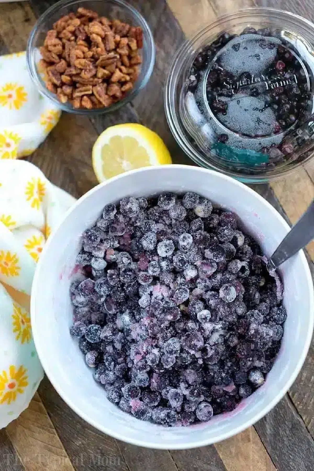 Huckleberry recipes you'll love. #huckleberries #jam #homemade #instantpot A bowl of frozen blueberries, a lemon half, a jar of pressure cooker jam, and a bowl of pecans rest on a wooden surface.