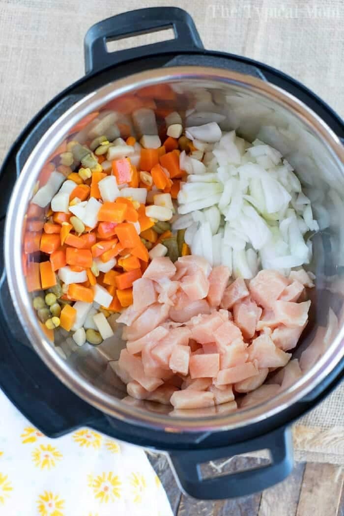 Chopped chicken, onions, and mixed vegetables in an Instant Pot, ready to be cooked into a hearty chicken pot pie soup.