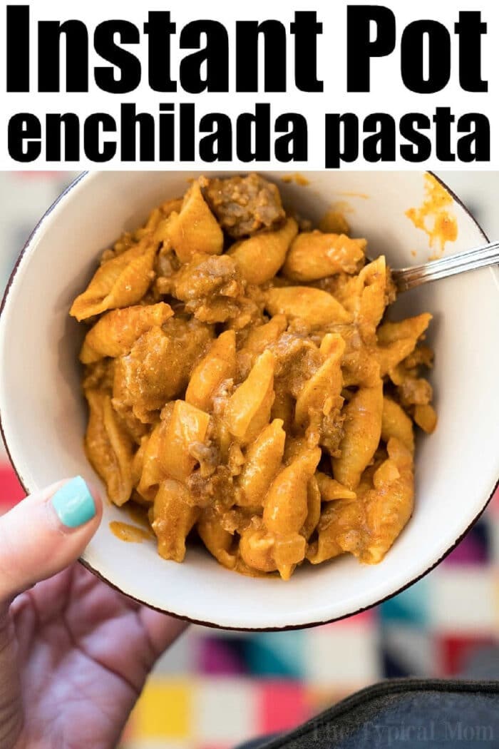 A bowl of cheesy enchilada pasta with shell noodles, inspired by instant pot enchilada casserole, held in one hand with a fork.