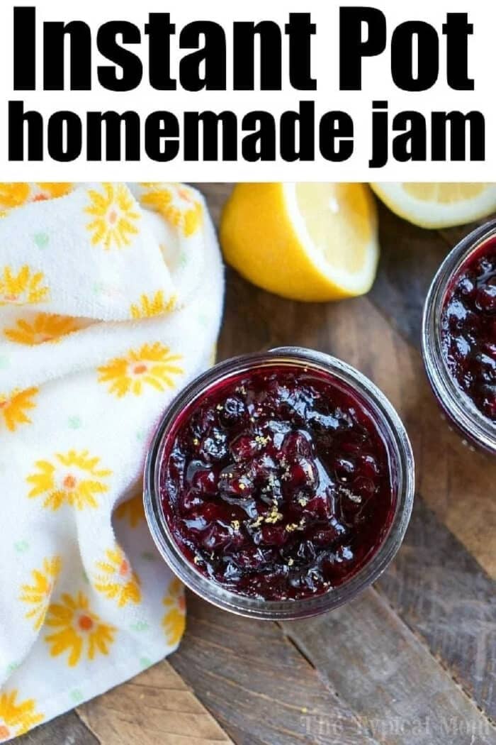 Pressure cooker jam takes 15 minutes and you can use any fruit you want. #instantpot #pressurecooker #jam #jelly #strawberry #huckleberry #homemade #berry #instantpotrecipes #thetypicalmom Two jars of homemade pressure cooker jam rest on a wooden surface, accompanied by a cut lemon and a floral towel.