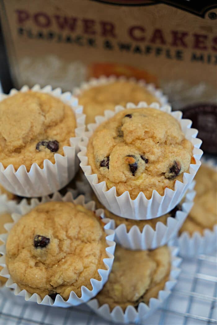 A stack of Kodiak Muffins in white paper liners sits in front of a box of pancake mix, tempting you with every chocolate chip.