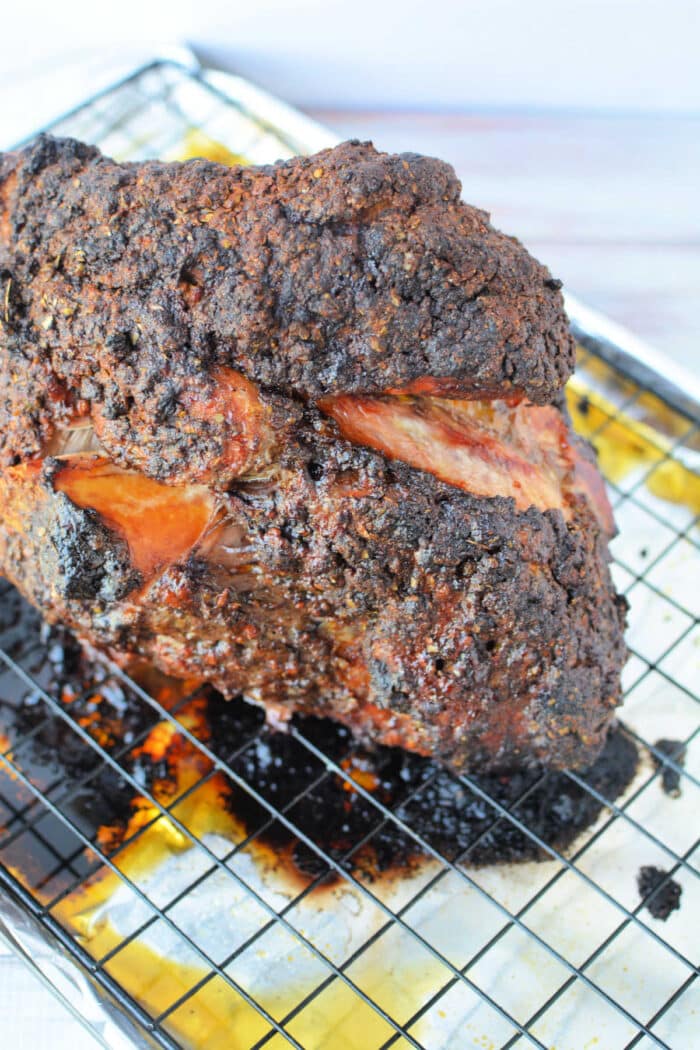 A large, crispy, blackened Pork Roast in Oven rests on a wire rack over a baking sheet with savory drippings.