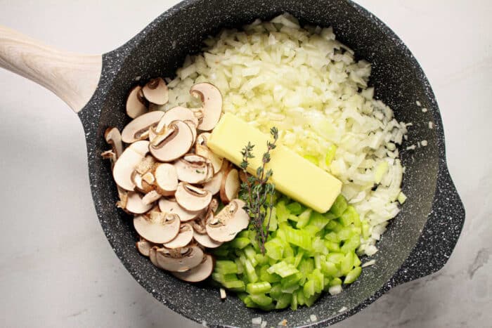Chopped onions, celery, mushrooms, butter, and thyme in a skillet, perfect as a base for Jiffy Cornbread Stuffing.