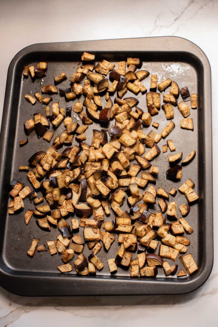 Chopped roasted eggplant pieces spread on a dark baking sheet hint at the perfect start to an irresistible eggplant casserole or your next favorite eggplant recipe.