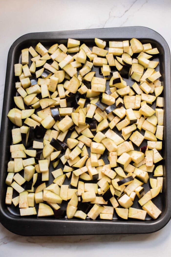 A baking tray filled with evenly spread, diced raw eggplant pieces on a light countertop—perfect for starting your favorite eggplant casserole or trying a new eggplant recipe.