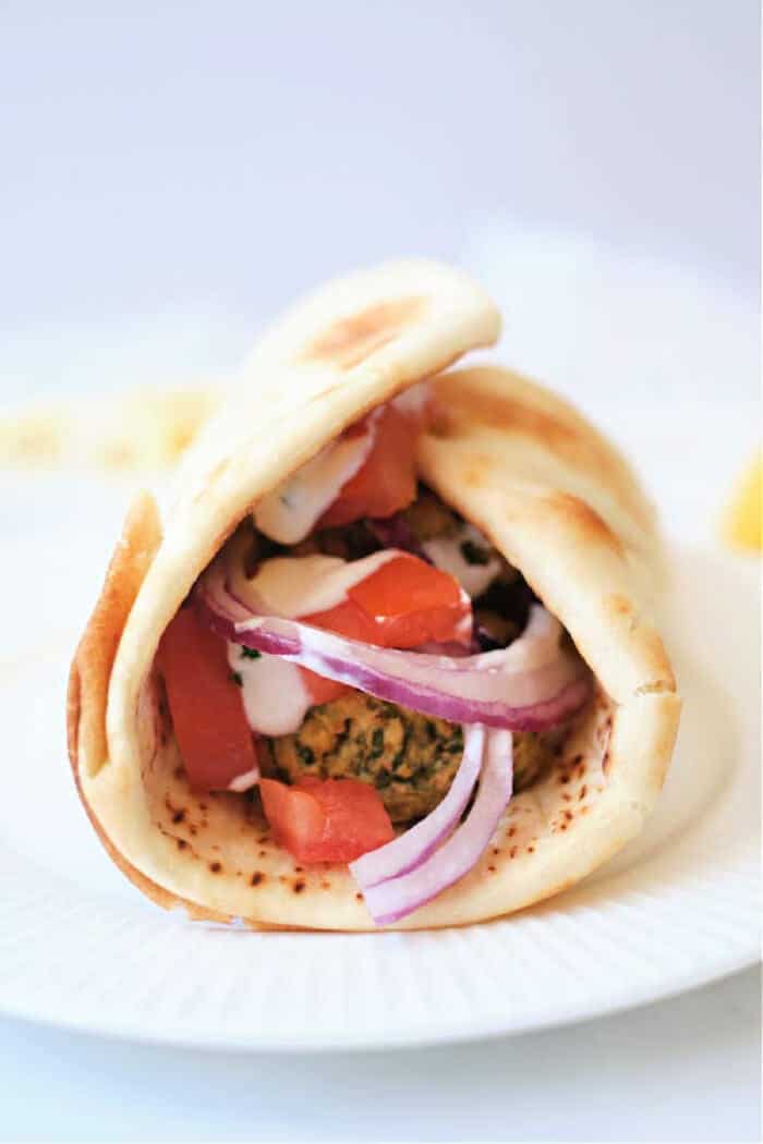 Pita wrap filled with air fryer falafel, sliced tomatoes, red onions, and creamy sauce on a white plate.