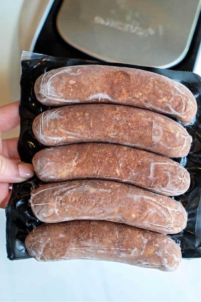 A hand holds a vacuum-sealed pack of five uncooked Italian sausages, perfect for cooking as flavorful Italian sausage in oven recipes.