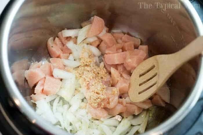 Chopped chicken, onions, and minced garlic simmer in a pot with a wooden spoon—the perfect start for an instant pot white chicken chili.