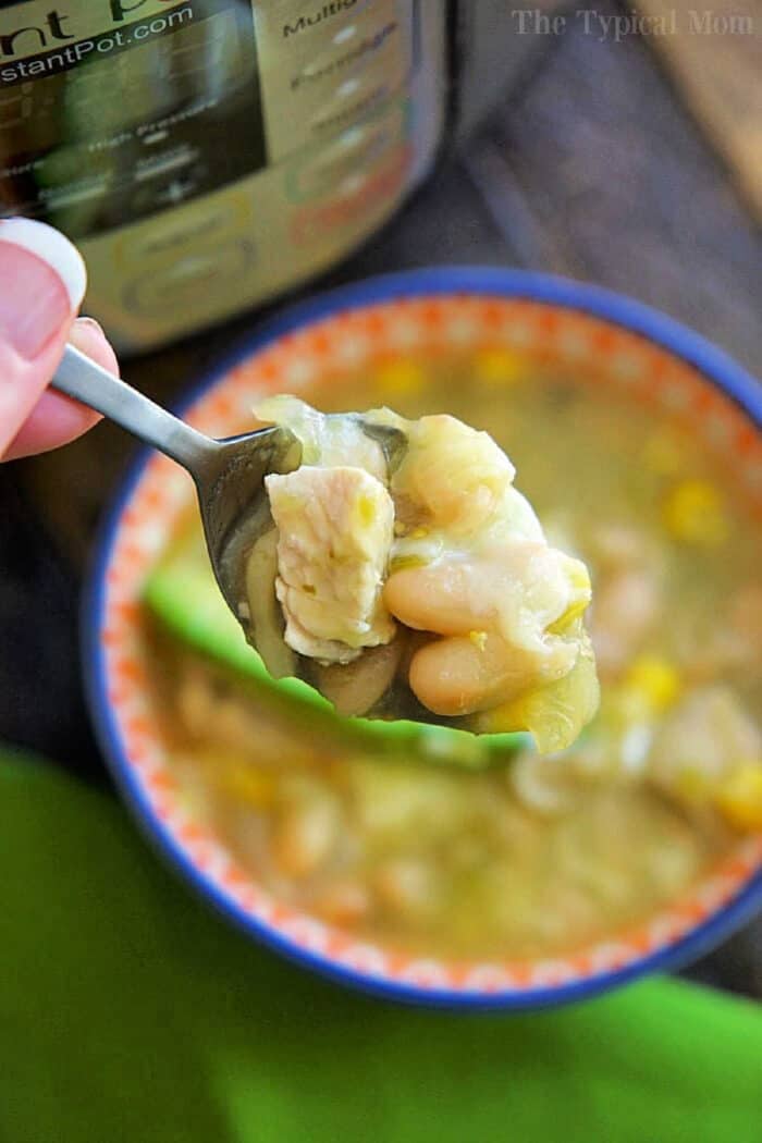 A spoonful of Instant Pot white chicken chili with beans held over a bowl, with an Instant Pot in the background.
