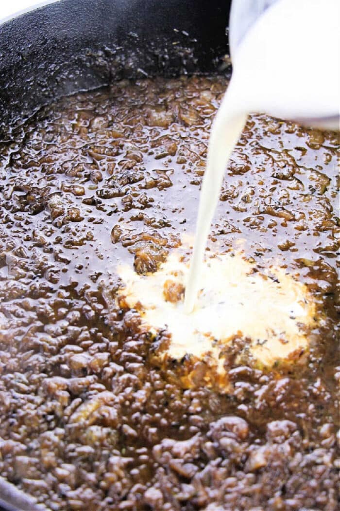 Cream being poured into a pan of browned ground beef, creating a creamy sauce that's perfect for an easy onion gravy recipe.