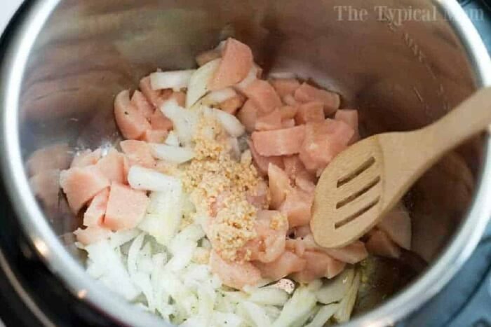 Chopped raw chicken, onions, and minced garlic in a pot with a wooden spoon&mdash;perfect for starting your instant pot white chicken chili.