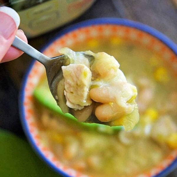 A spoonful of Instant Pot white chicken chili held above a bowl, with the pressure cooker in the background.