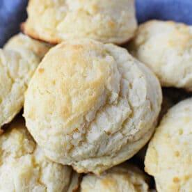 A close-up of freshly baked, golden-brown sour cream biscuits stacked on a blue cloth.