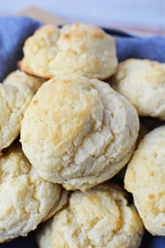 A close-up of freshly baked, golden-brown sour cream biscuits stacked on a blue cloth.