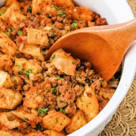 A wooden spoon in a bowl of savory chorizo stuffing, mixed with herbs and sausage.
