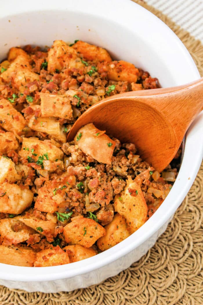 A wooden spoon in a bowl of savory chorizo stuffing, mixed with herbs and sausage.