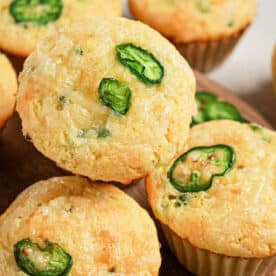 Corn muffins topped with slices of fresh jalapeños, made using a classic Jiffy Corn Muffins recipe, arranged on a wooden surface.
