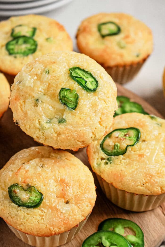 Corn muffins topped with slices of fresh jalapeños, made using a classic Jiffy Corn Muffins recipe, arranged on a wooden surface.