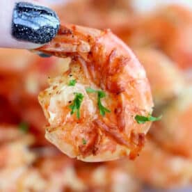 A hand with black glittery nails holds a cooked shrimp garnished with herbs, freshly made from air fryer frozen shrimp.