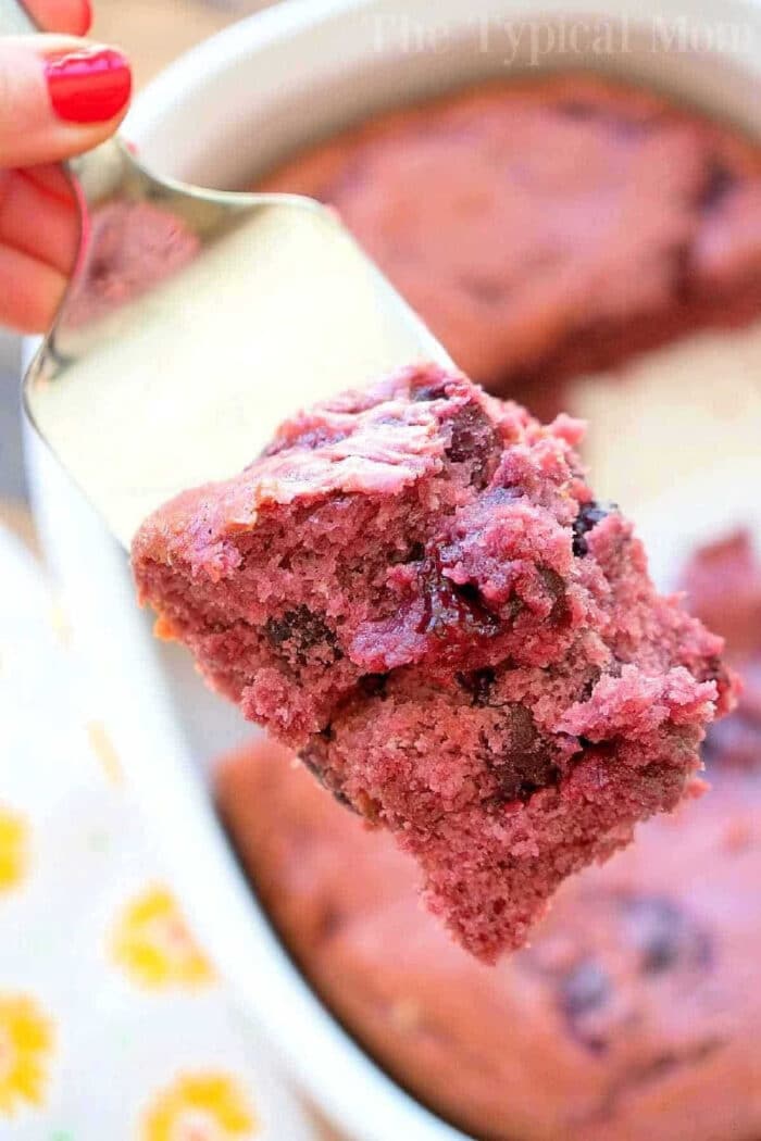 You've got to try this easy 3 ingredient cherry pie filling dump cake for dessert! It's so simple to make even your kids can throw it together. It's really moist and packed with dark cherries or any other pie filling flavor you love. Cake mix baking has never been easier with this fun dump cake recipe. #cherry #pie #cake #dump #blueberry #easy #piefilling #cakemix #recipes A close-up of a spatula holding a piece of cherry pie filling dump cake above a baking dish.