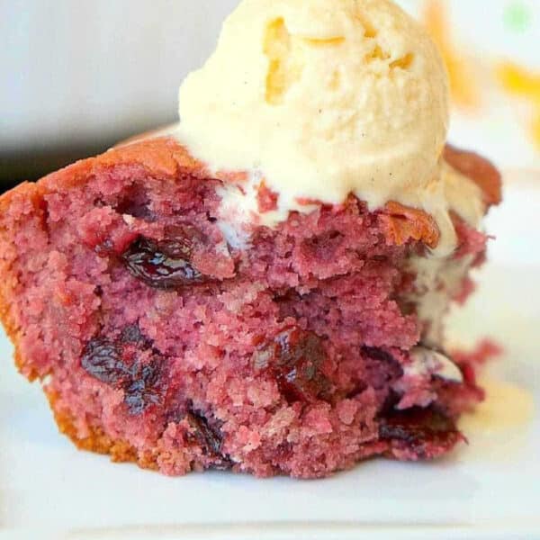 A slice of berry cake made with cherry pie filling dump cake, topped with a scoop of vanilla ice cream on a white plate.