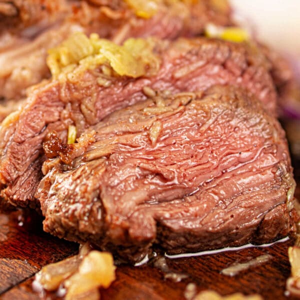 Close-up of juicy, sliced chuck roll steak topped with onions on a wooden cutting board.
