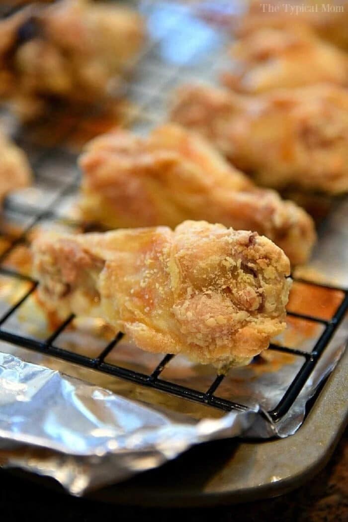 A baked chicken wing rests on a wire rack over a foil-lined baking sheet, showing how to bake crispy chicken wings with perfectly golden skin.