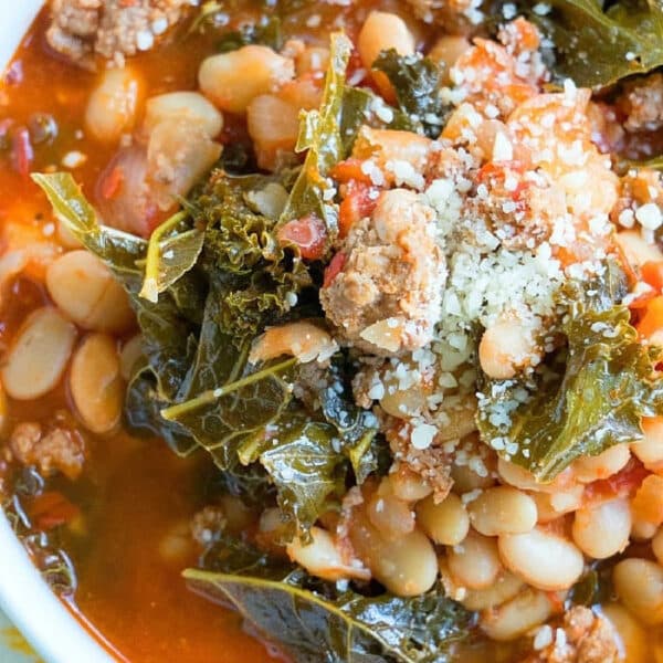 A bowl of hearty pressure cooker sausage soup with beans, kale, ground meat, tomato broth, and grated cheese on top.