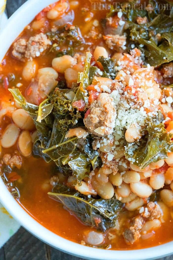 A bowl of hearty pressure cooker sausage soup with beans, kale, ground meat, tomato broth, and grated cheese on top.