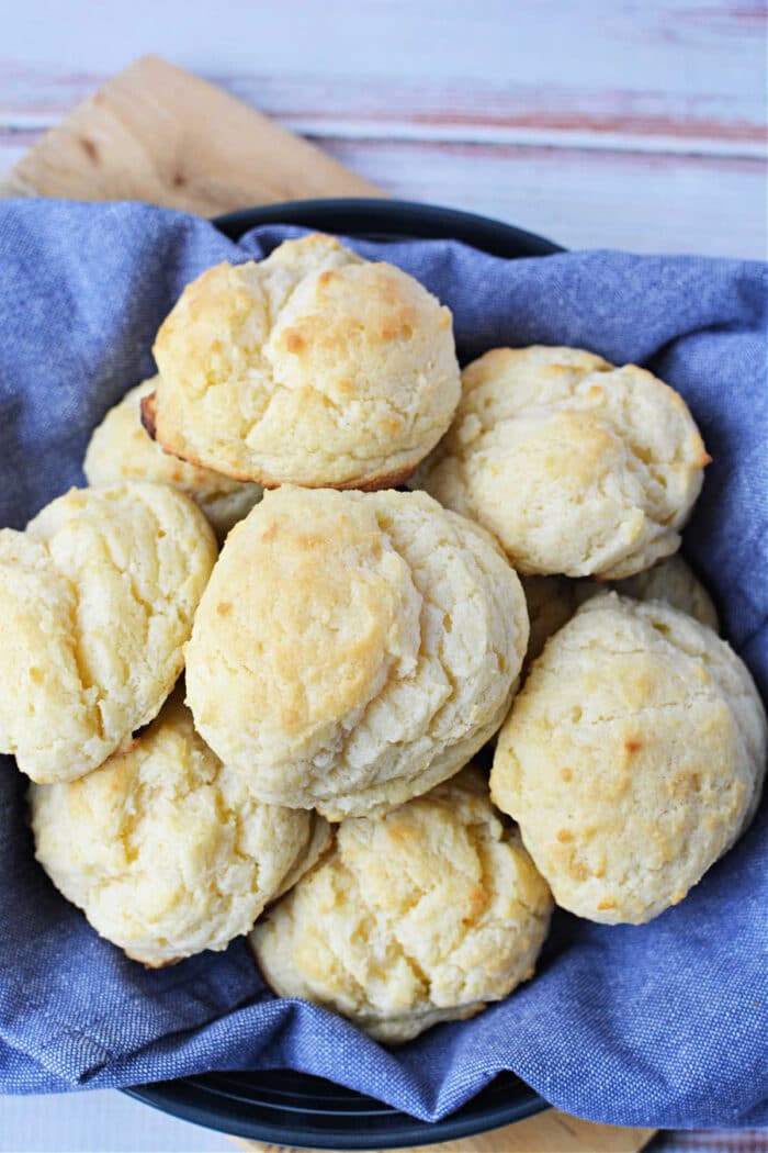 A basket lined with blue cloth holds several golden, fluffy sour cream biscuits—a perfect treat for anyone searching for the ultimate biscuits recipe.