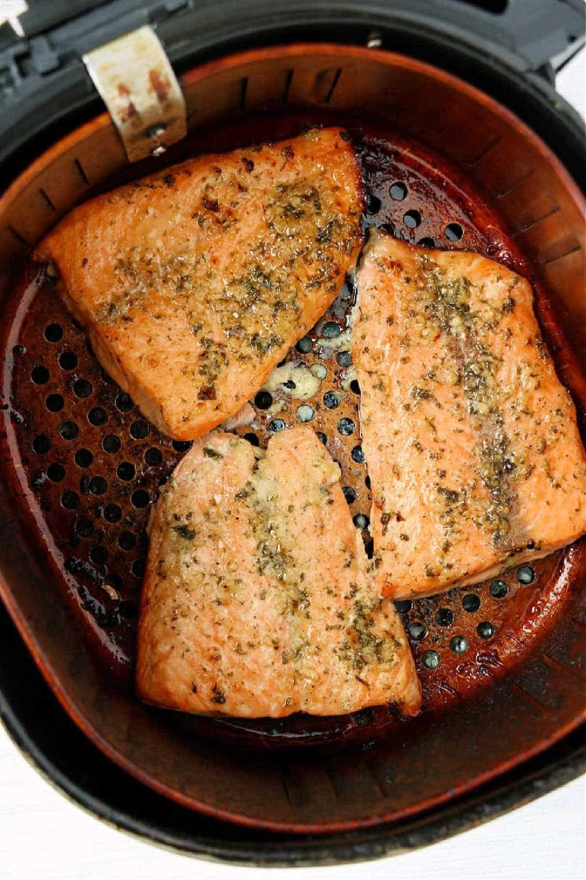 Three seasoned frozen salmon fillets cooked in an air fryer basket, showing a perfectly golden-brown exterior.