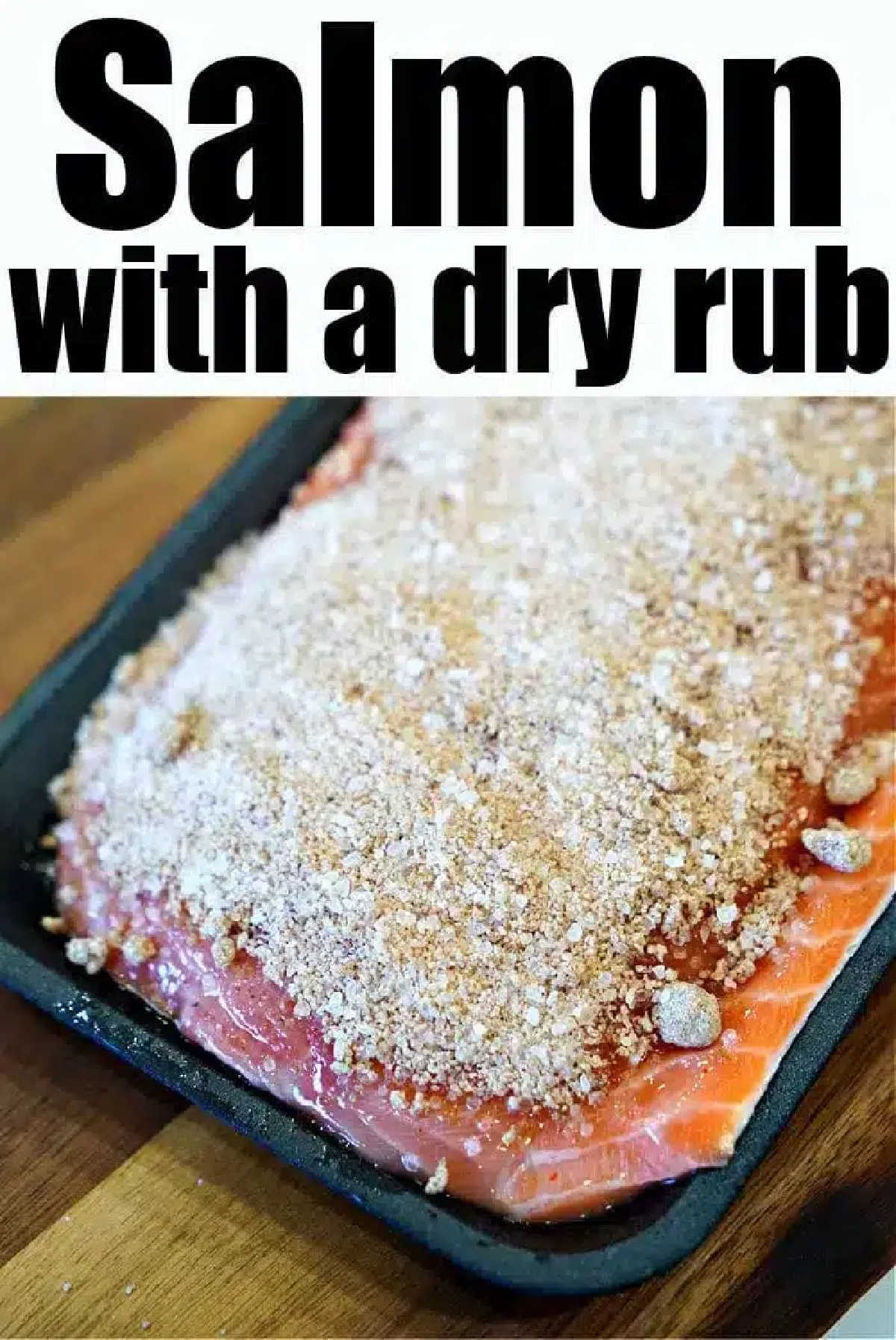 Raw salmon fillet in a pan covered with a dry seasoning rub, ready to become the best baked salmon, on a wooden surface.
