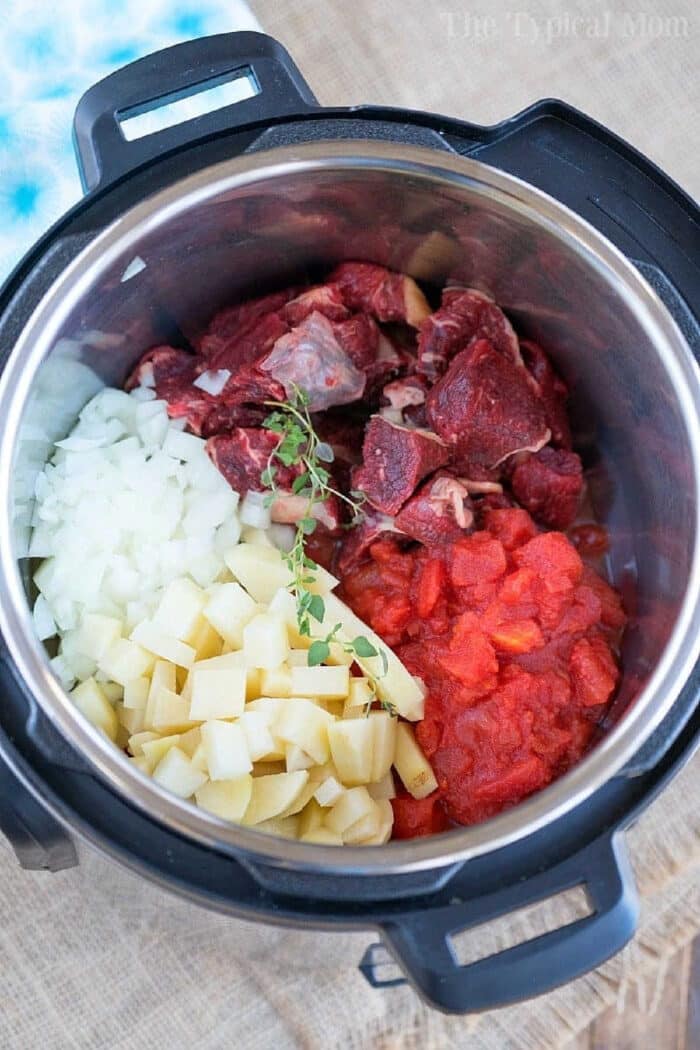 Chopped beef, onions, potatoes, tomatoes, and herbs in a pressure cooker for a comforting beef pot pie soup ready to be cooked.