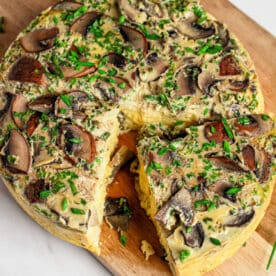 A sliced mushroom and herb frittata, inspired by an Instant Pot Quiche, sits on a wooden board with fresh chives sprinkled on top.