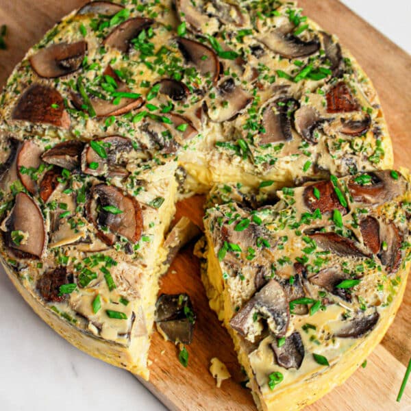 A sliced mushroom and herb frittata, inspired by an Instant Pot Quiche, sits on a wooden board with fresh chives sprinkled on top.
