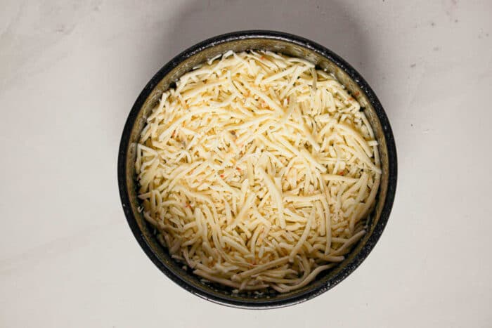 A black bowl filled with shredded cheese on a white marble surface, perfect for adding to your favorite Quiche or Instant Pot Quiche recipe.