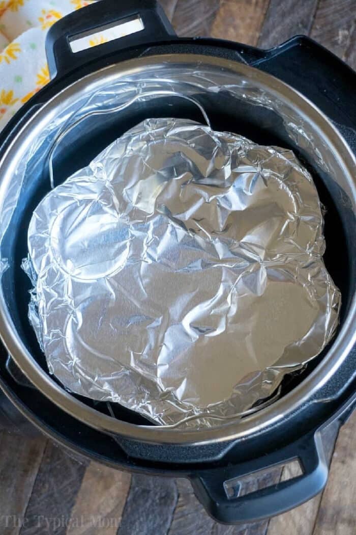Pressure cooker egg bites are the perfect protein packed breakfast for busy mornings. A great Keto Instant Pot recipe with just a few ingredients. #instantpot #eggbites #starbucks #keto #instantpotrecipes #pressurecooker #crockpotexpress #thetypicalmom Aluminum foil covers food inside an Instant Pot on a wooden surface, perfect for making pressure cooker egg bites.
