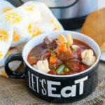 Bowl of pressure cooker beef pot pie soup with crackers, next to bread and a yellow-patterned napkin.