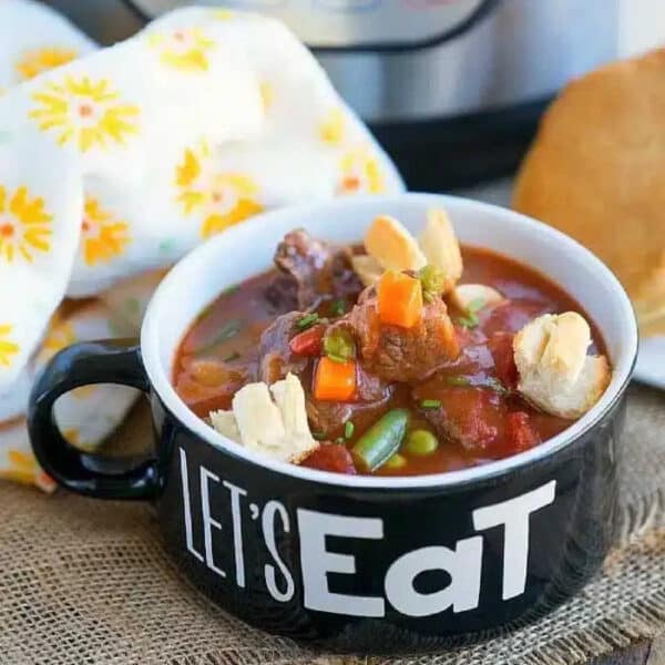 Bowl of pressure cooker beef pot pie soup with crackers, next to bread and a yellow-patterned napkin.