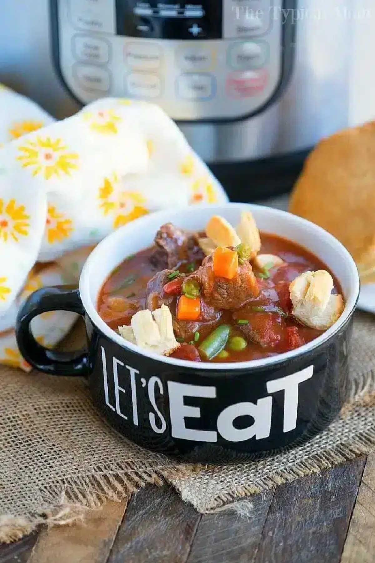 Bowl of pressure cooker beef pot pie soup with crackers, next to bread and a yellow-patterned napkin.