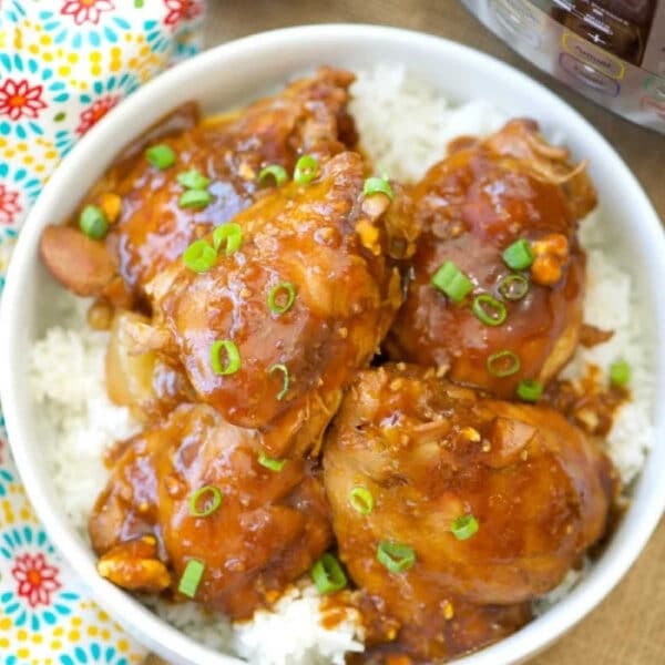 Bowl of saucy Instant Pot spicy teriyaki chicken thighs on white rice, garnished with chopped green onions, next to a pressure cooker.