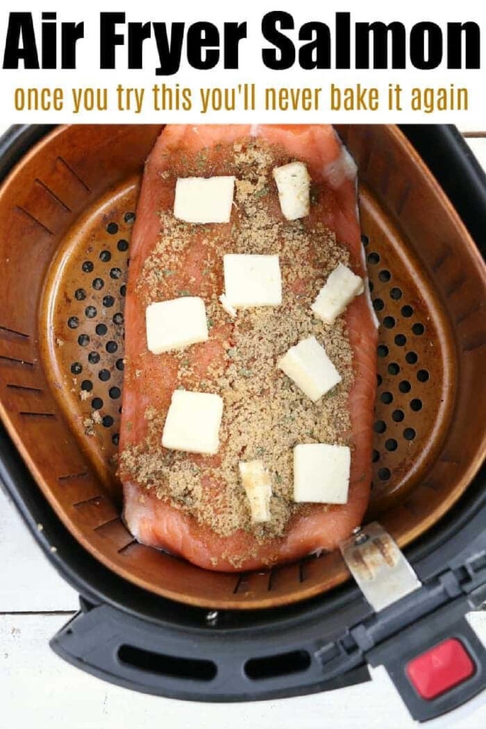 Salmon in the air fryer is amazing! With a sweet glaze on top cooking fish in a Ninja Foodi or other brand is easy and a healthy dinner you'll love. #ninjafoodirecipes #salmon #airfryerrecipes #airfryersalmon #fish #foodi #ninjafoodi #thetypicalmom Salmon filet with seasoning and butter cubes in an air fryer basket, ready to be cooked—perfect for making delicious salmon in the air fryer.